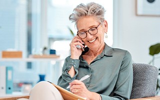 Woman smiling while talking on phone and taking notes