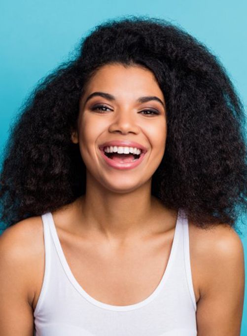 woman with dental crowns in Lakewood, Dallas, TX in front of a turquoise background 