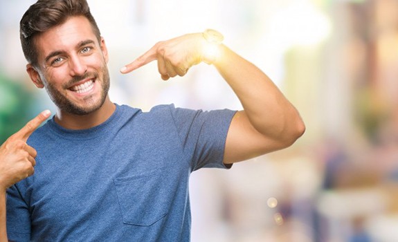 man in a blue shirt pointing to his smile 