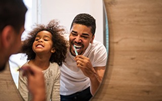 Father and daughter brushing their teeth together
