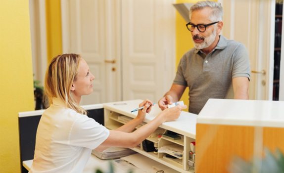 Man at dental office front desk, paying for treatment