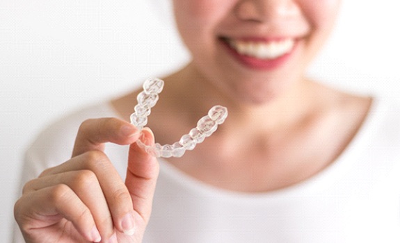 A smiling woman holding up an Invisalign aligner tray 