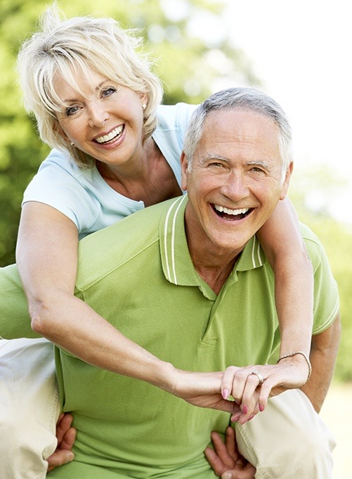 Older man and woman smiling after replacing missing teeth