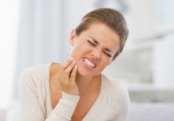 Woman in need of restorative dentistry holding cheek in pain
