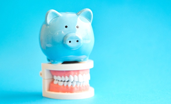 Piggy bank atop model teeth representing the cost of smile makeovers in Lakewood