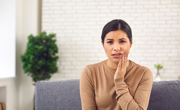 a person sitting on their couch and holding their mouth in pain