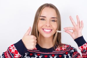 woman wearing holiday sweater and holding Invisalign tray