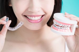 Nose to chin view of woman holding clear aligner in one hand and braces in the other